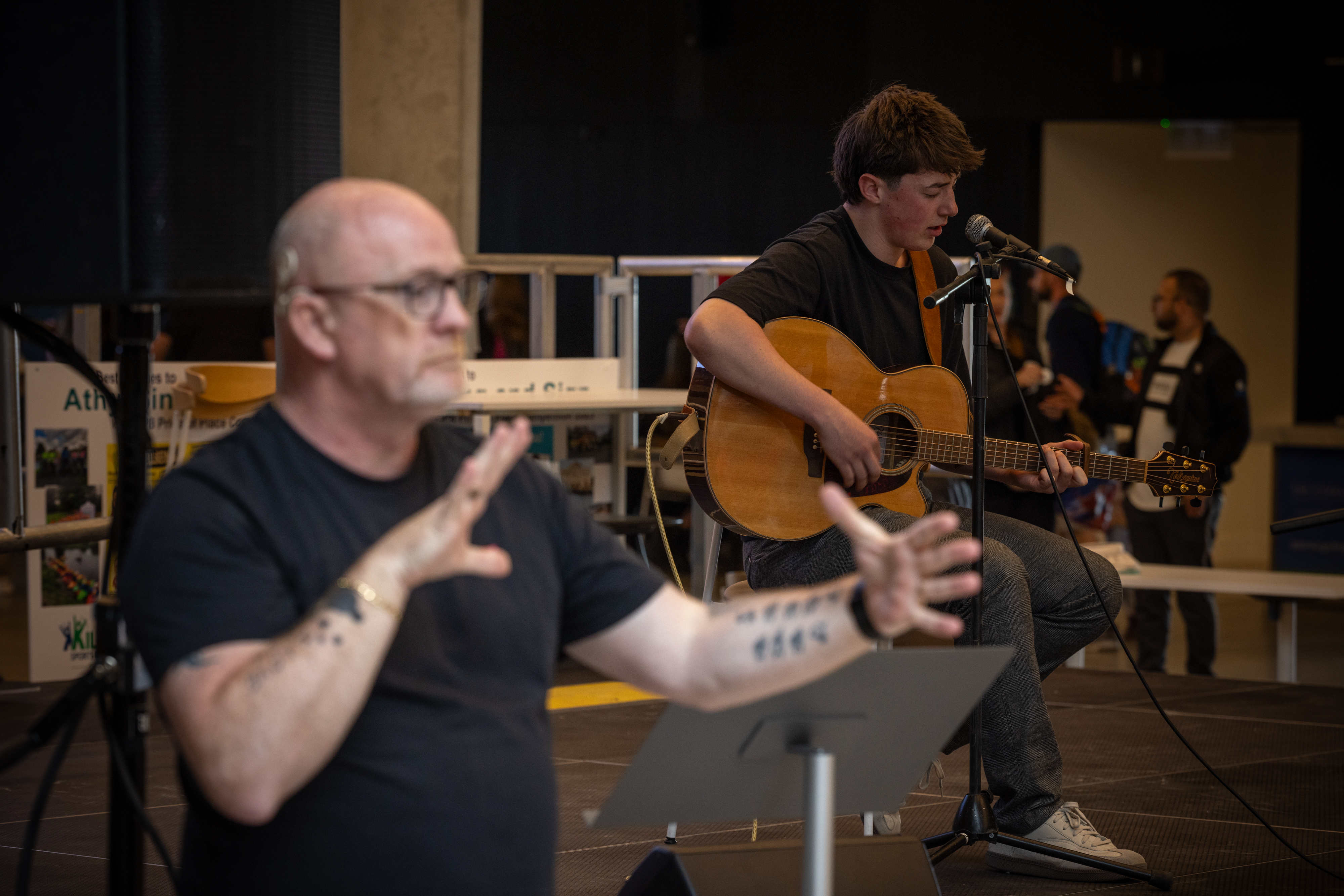 A person singing on stage with playing guitar , accompanied by a sign language interpreter. 